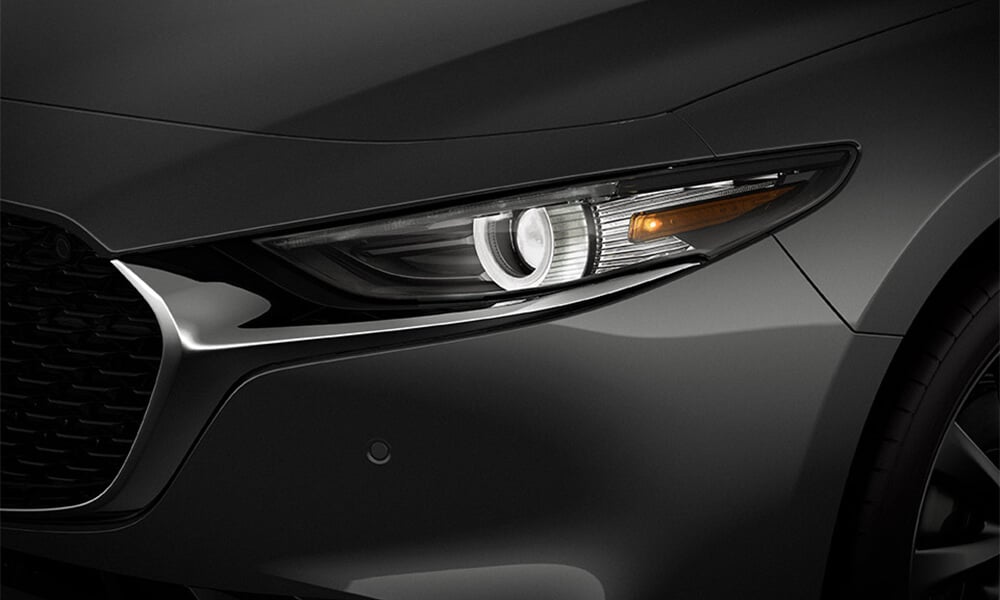 Close-up of a Machine Grey Metallic Mazda3 headlight.
